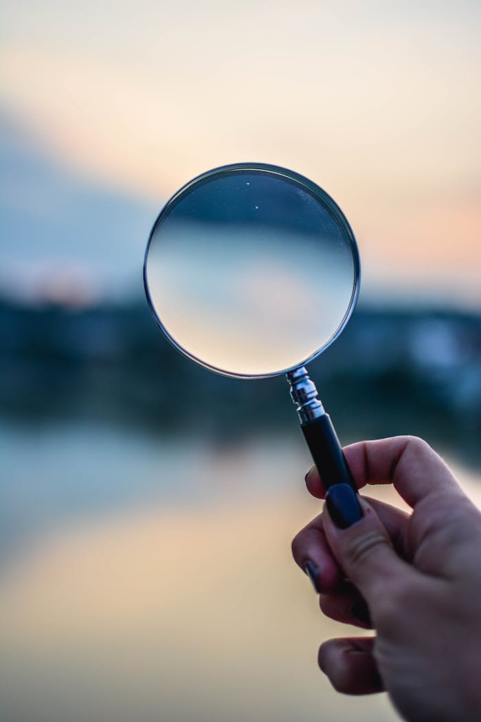 services-04 A magnifying glass held by a hand outdoors at sunset, focusing on exploration.