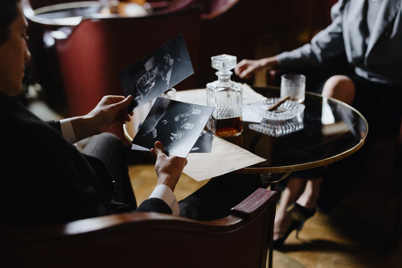 heros-img A detective analyzes black-and-white photos with a whiskey decanter and cigar on a table, creating a classic noir ambiance.